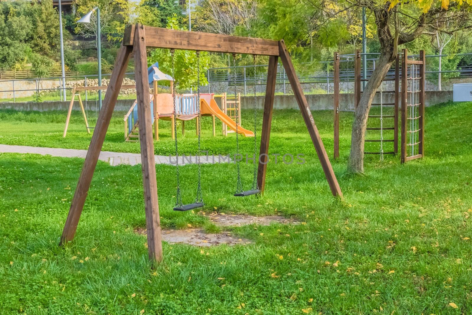 empty swings at playground for child near children stairs slides equipment, on green meadow background