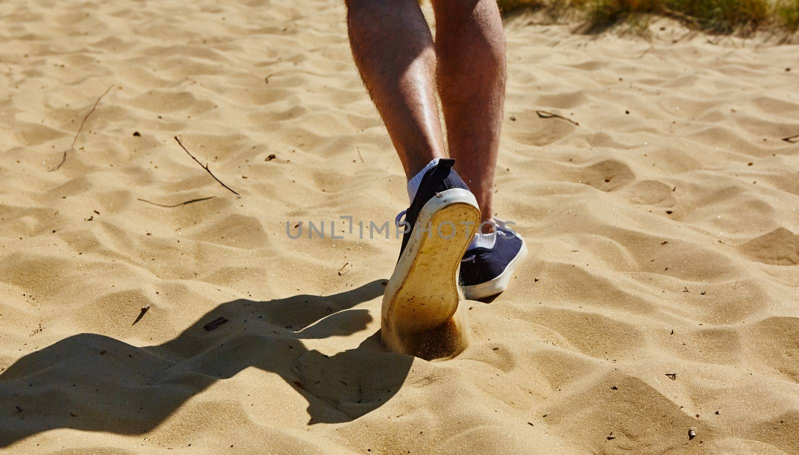 Close up fashion image of man walking alone at tropical exotic beach with blue ocean and white sand, wearing stylish sneakers.