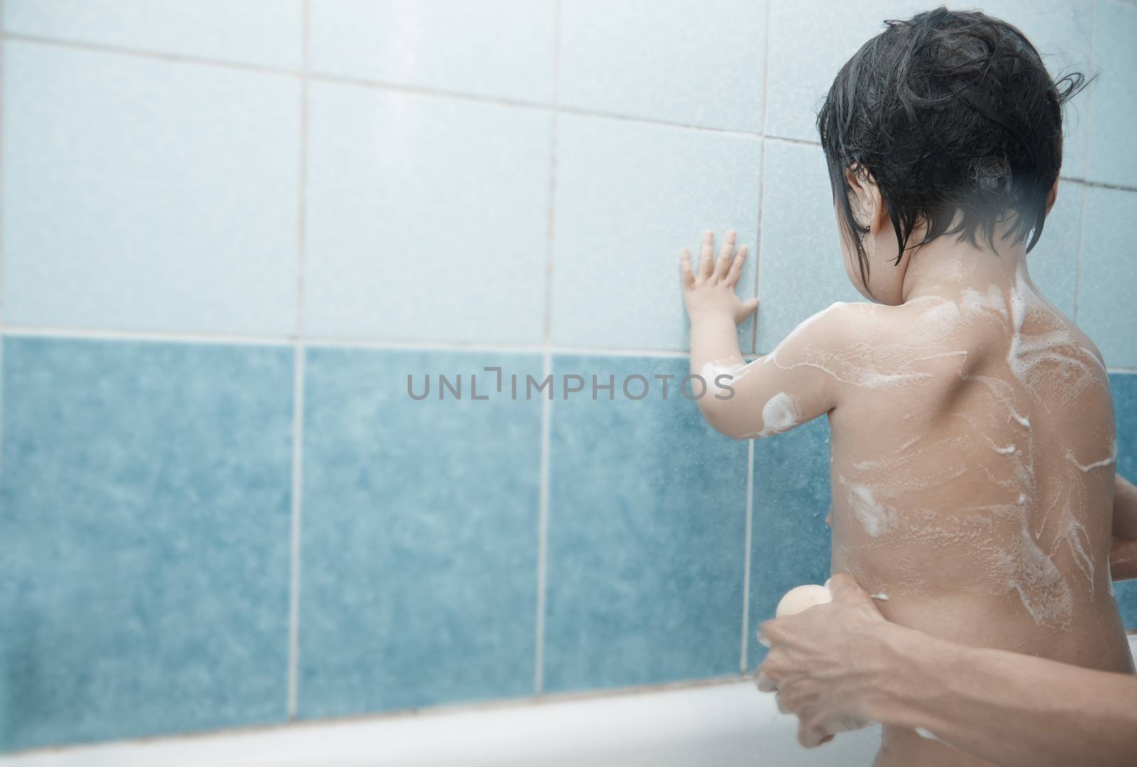 Mothers hands lathering child in the bath. Horizontal photo