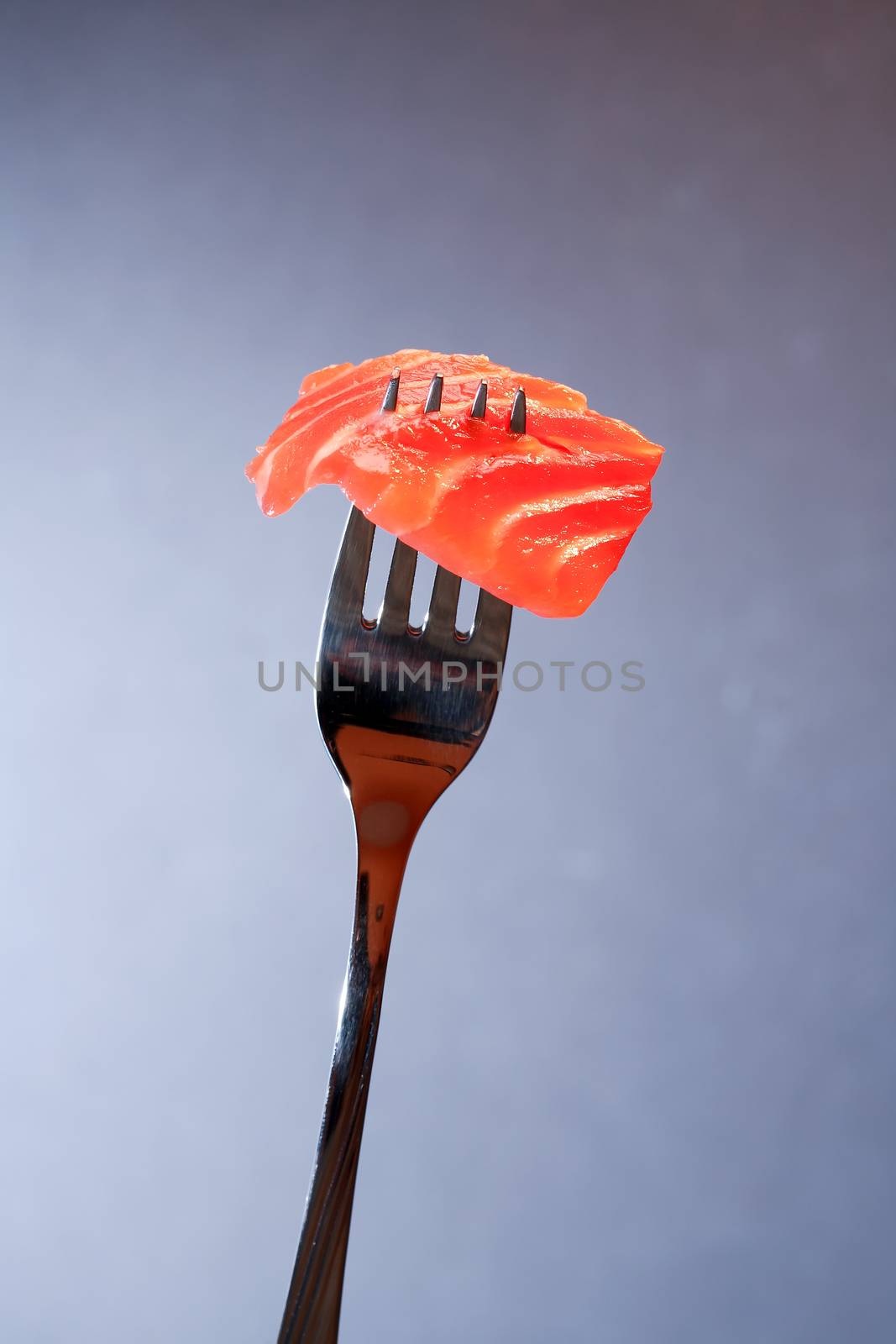 Closeup of steel fork with slice of salmon on dark background