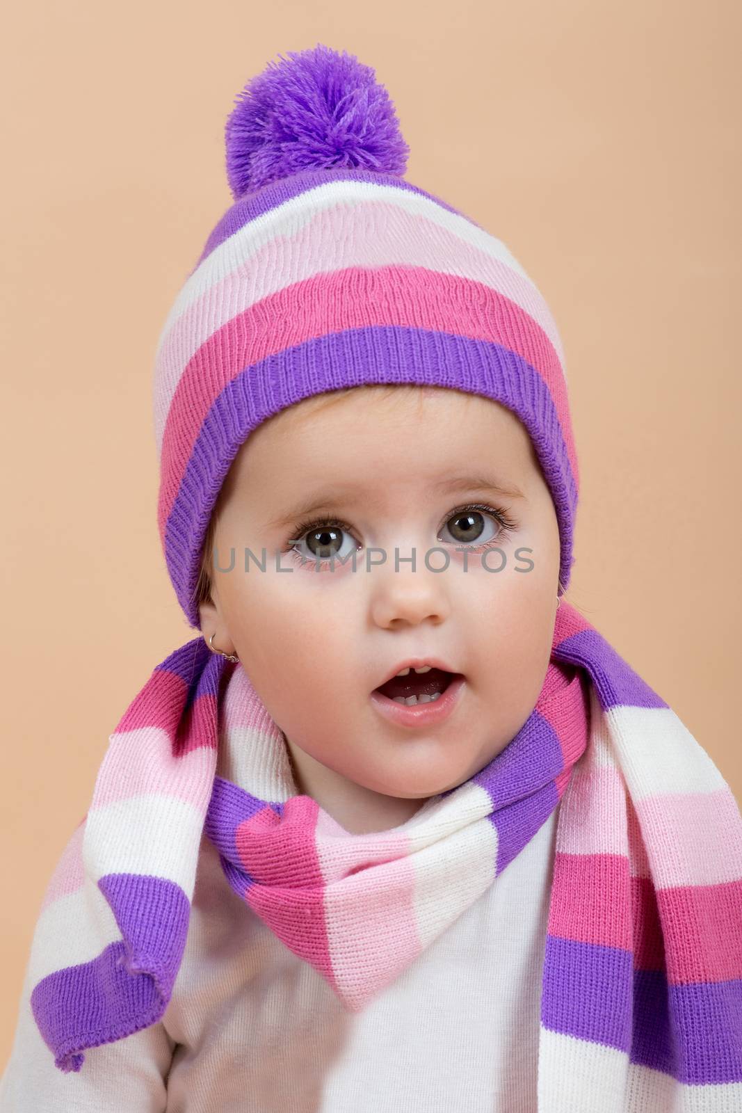 portrait of young cute baby with winter cap and scarf on beige background