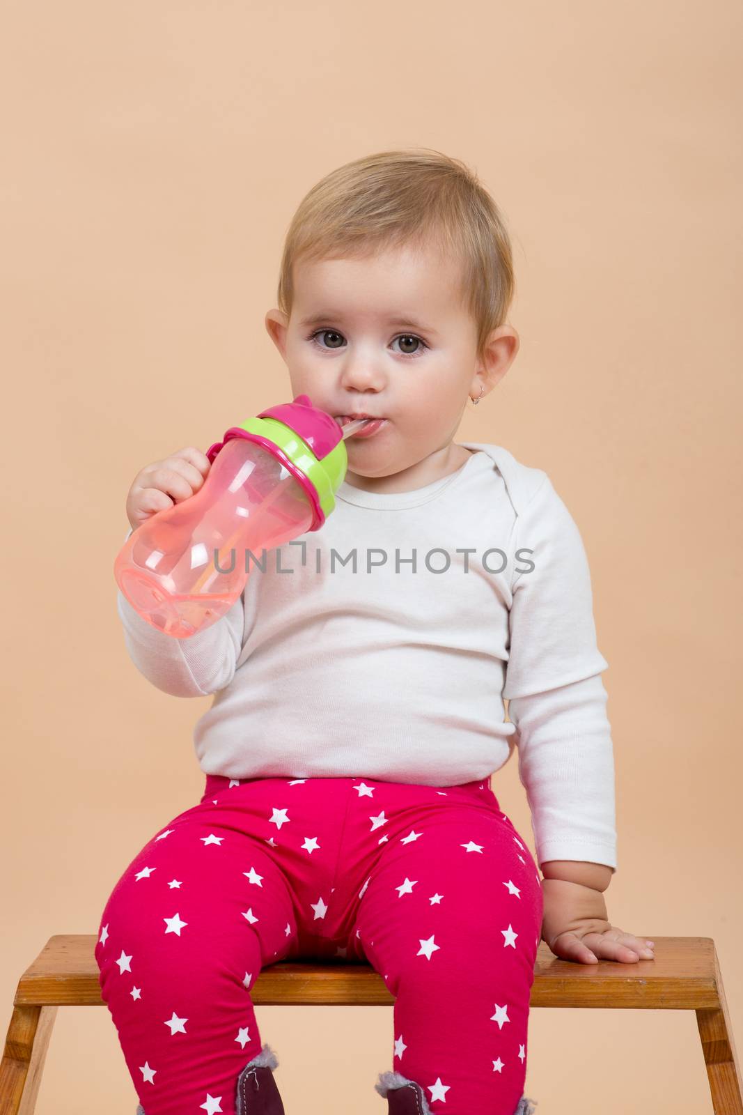 portrait of young cute baby with on beige background with bottle