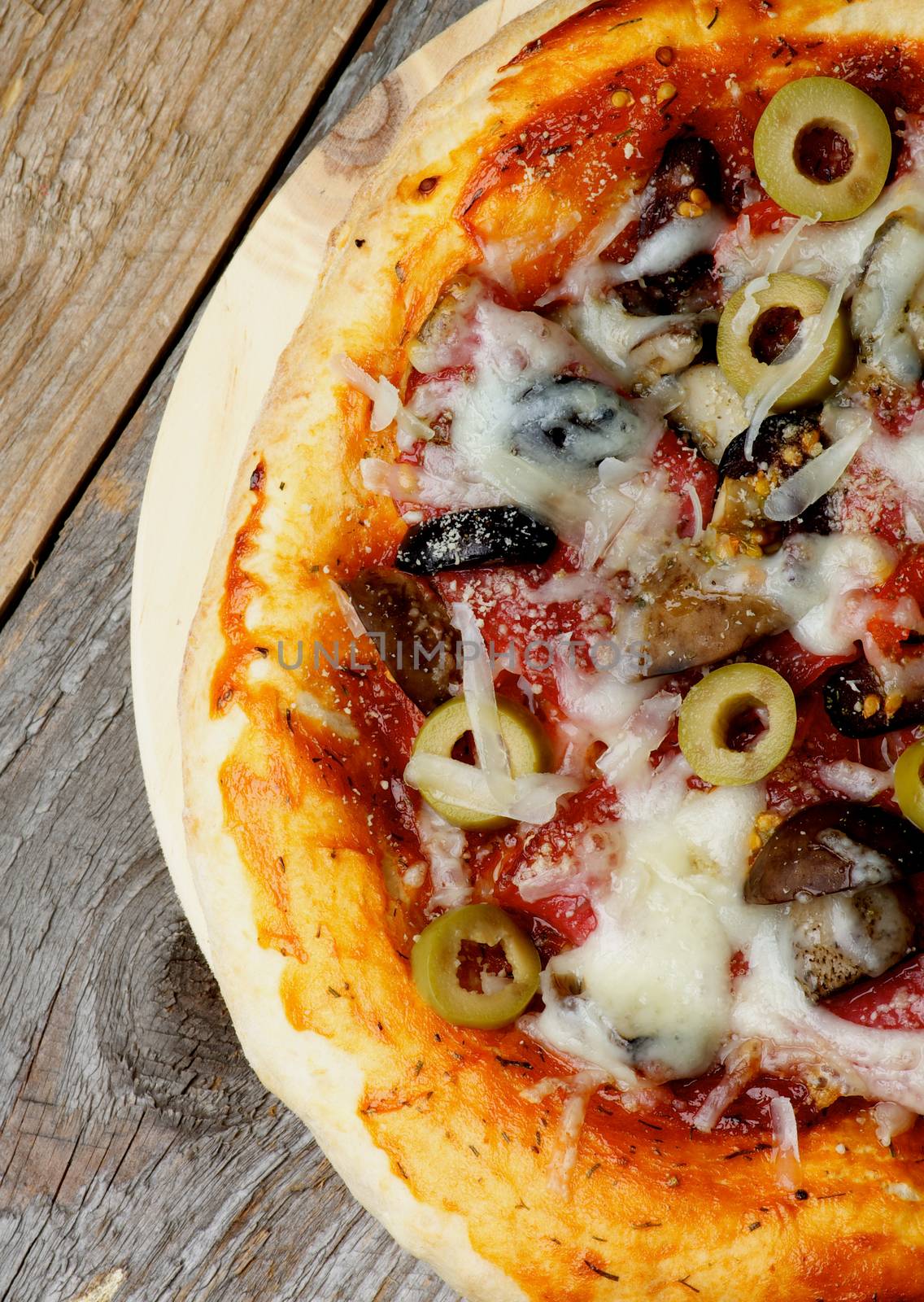 Homemade Mushroom and Olives Pizza with Tomatoes, Salami and Grated Cheese on Circle Cutting Board Cross Section on Wooden background. Top View