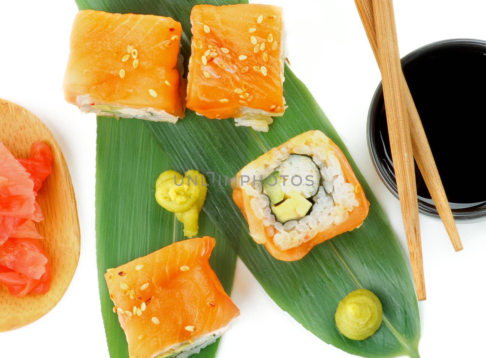 Delicious Salmon Maki Sushi with Crab, Avocado and Cheese on Green Palm Leafs with Soy Sauce, Ginger and Pair of Chopsticks closeup on white background. Top View
