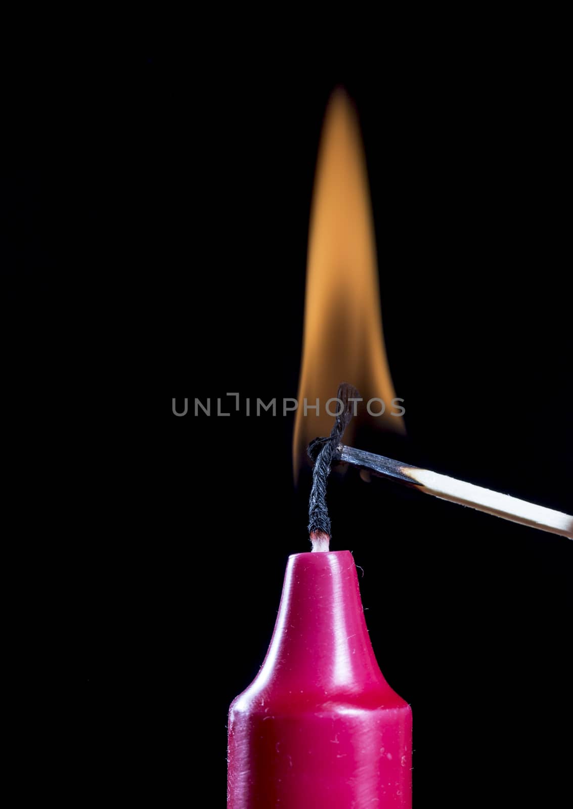 Red Candle Stick Burning with match and black background.
