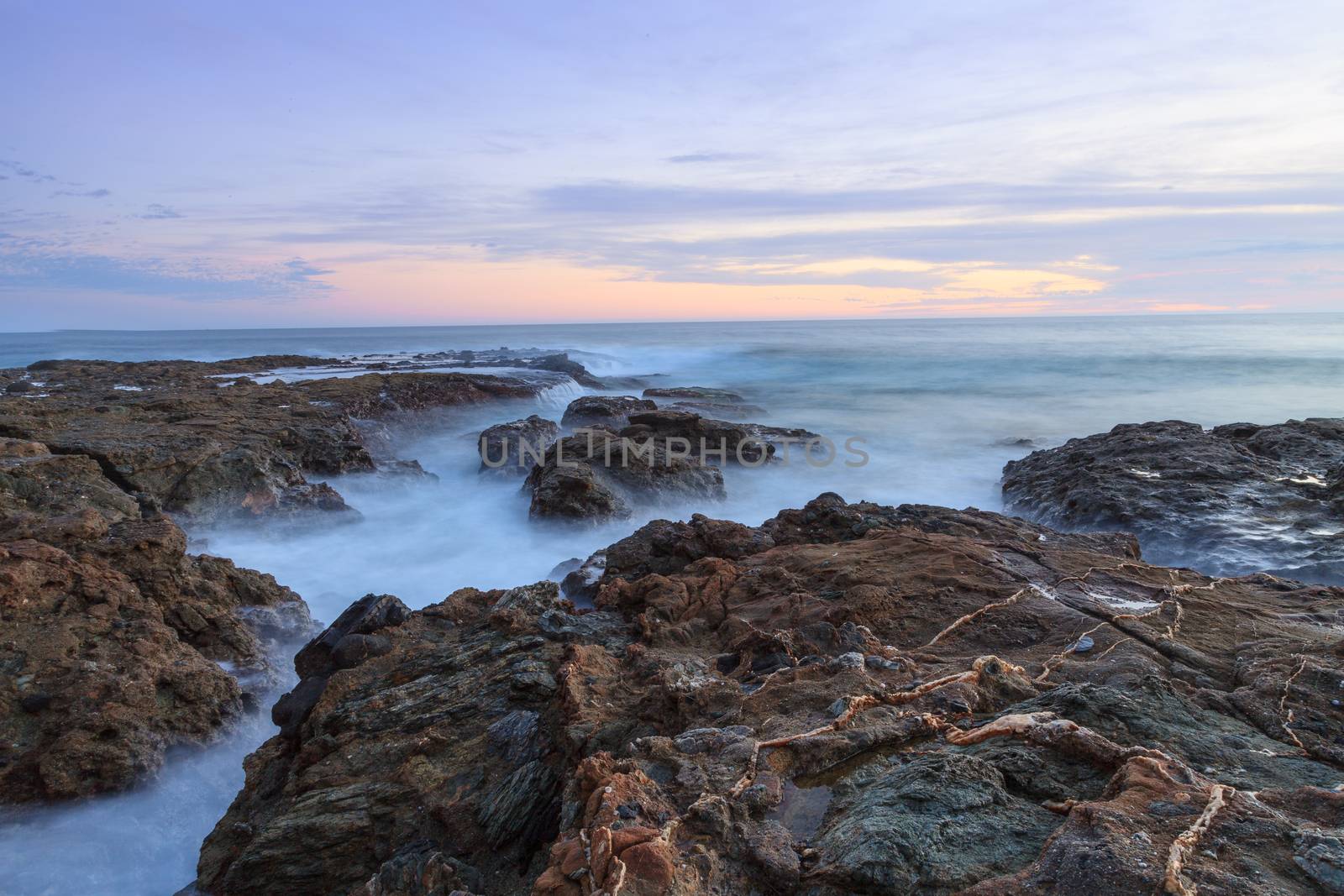 Long exposure of rocks in waves, giving a mist like effect over ocean in Laguna Beach, California at sunset