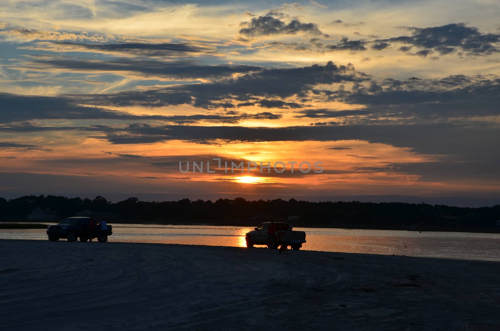 Two cars parked on the beach watching the sunset.