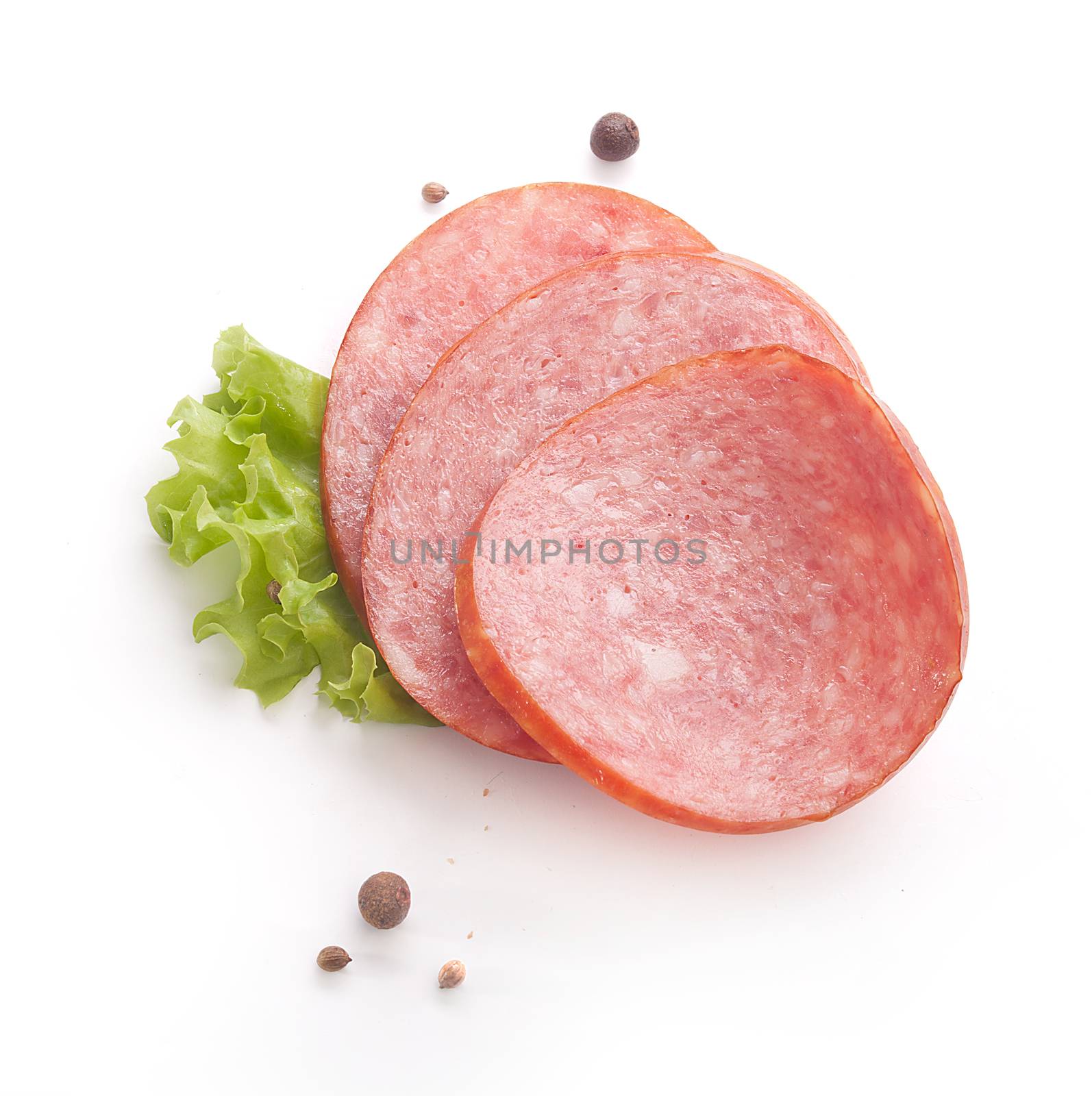 Three pieces pf smoked sausage with fresh green lettuce and black pepper on the white