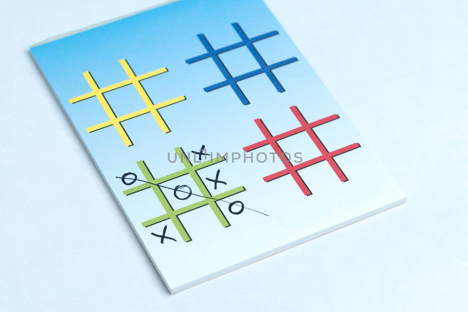 A close up of a game of Xs and Os on a note pad with colorful grids made for playing.