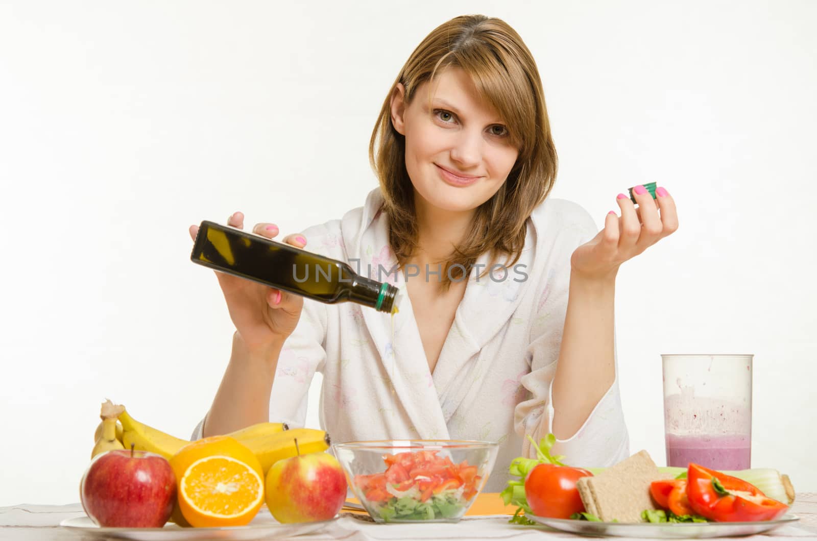 Young beautiful girl in a bathrobe prepares vegetarian salad from vegetables and greens isolated on white background