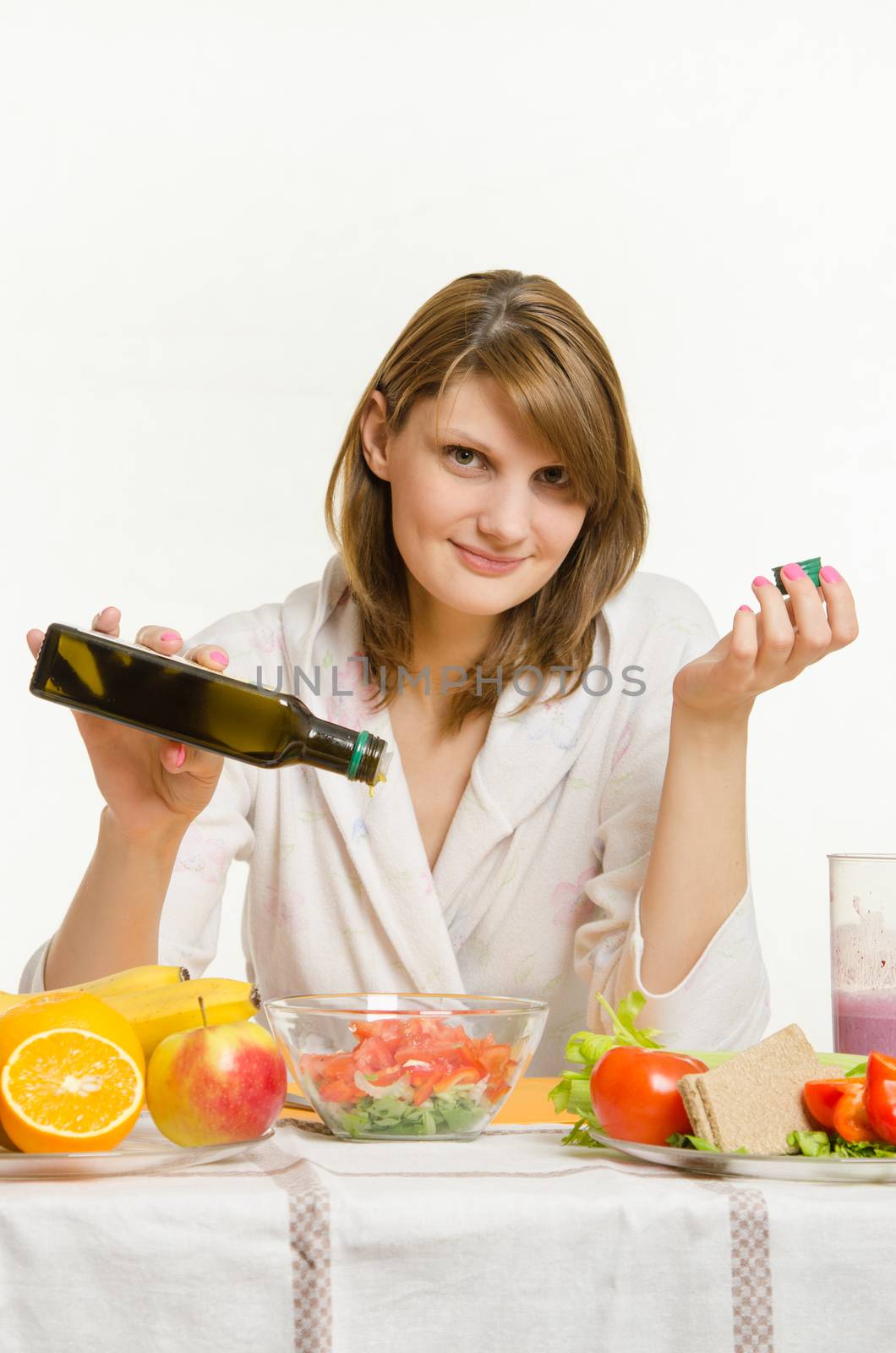Young beautiful girl in a bathrobe prepares vegetarian salad from vegetables and greens isolated on white background