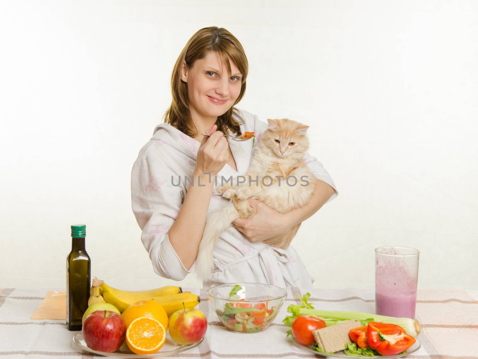 Young beautiful girl in a bathrobe prepares vegetarian salad from vegetables and greens isolated on white background