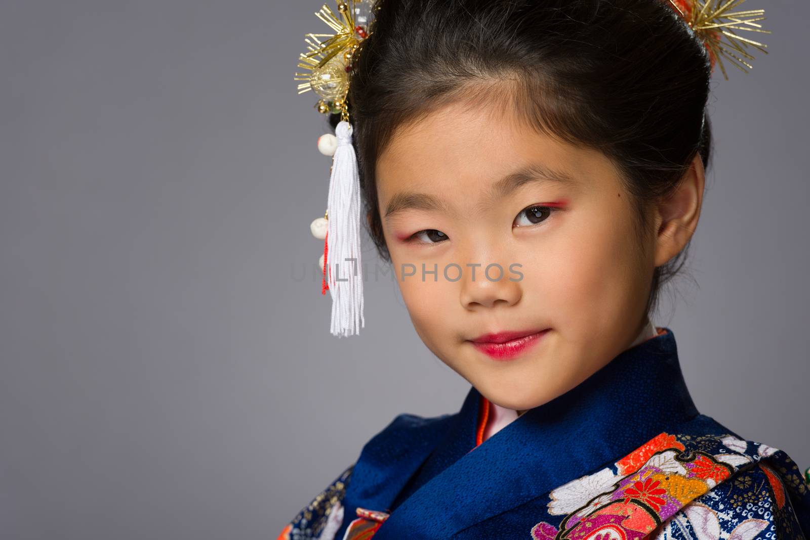 A cute young Japanese girl wearing a Kimono on a grey background.