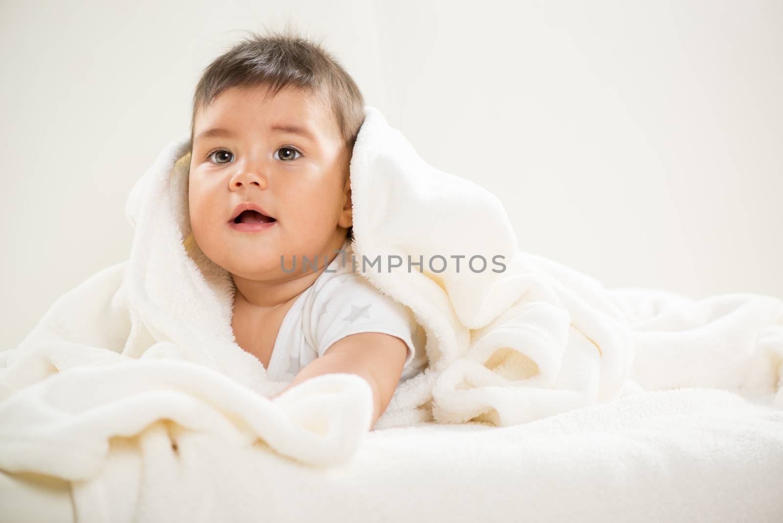 Cute baby boy lying under a blanket playfully and exploring his world