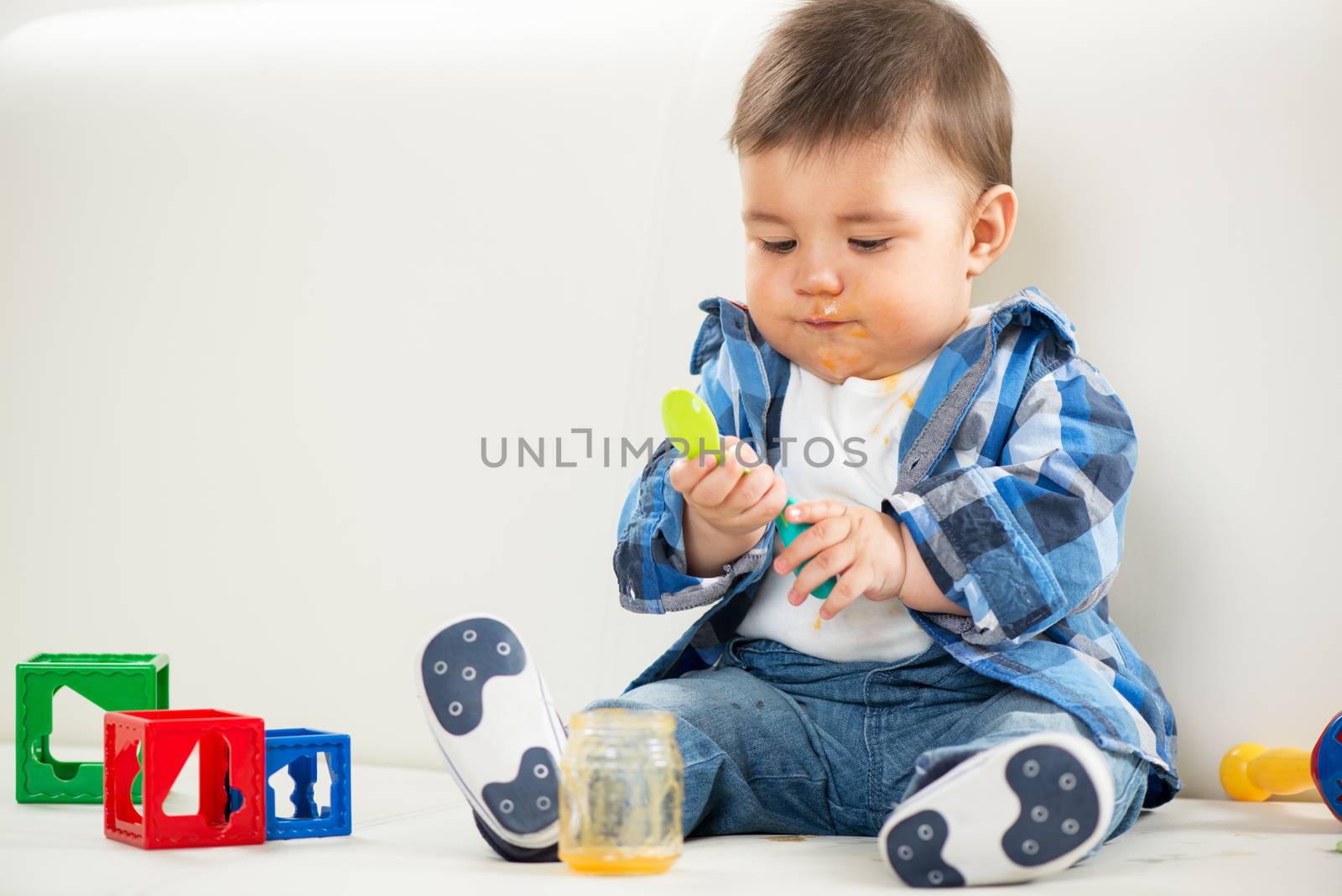 Cute baby boy sitting at home and playing with spoon