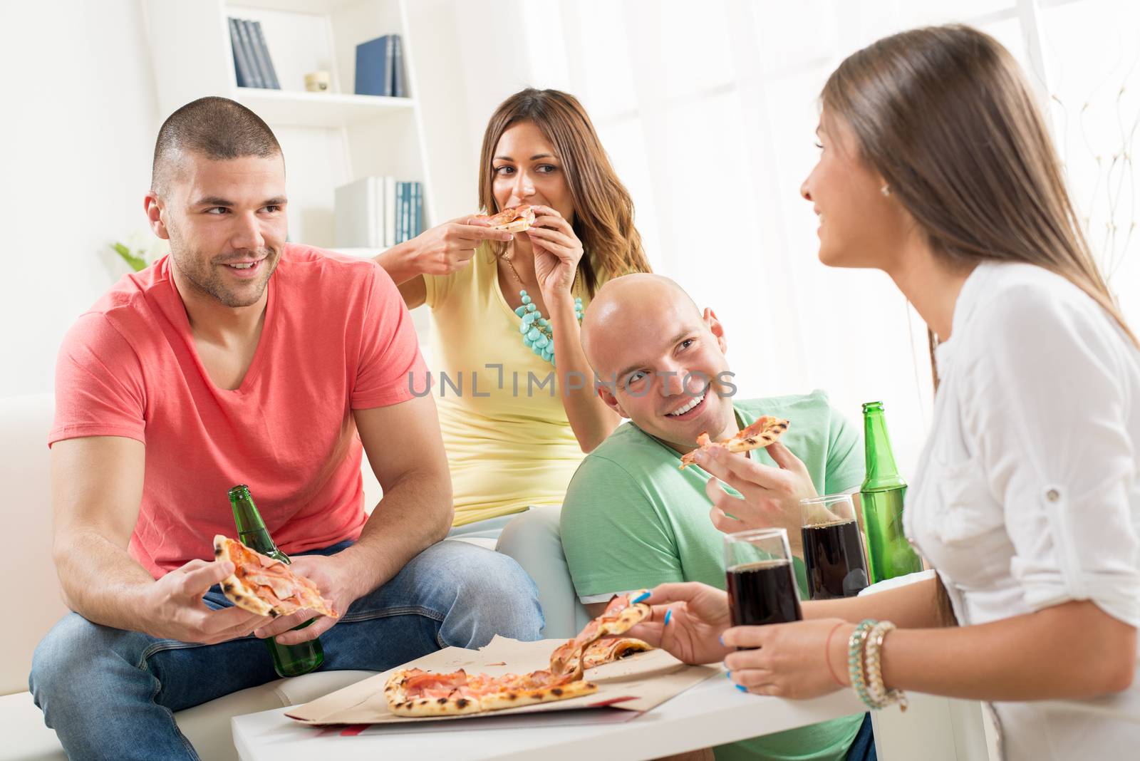 Friends enjoying eating pizza and drink a beer together at home party.