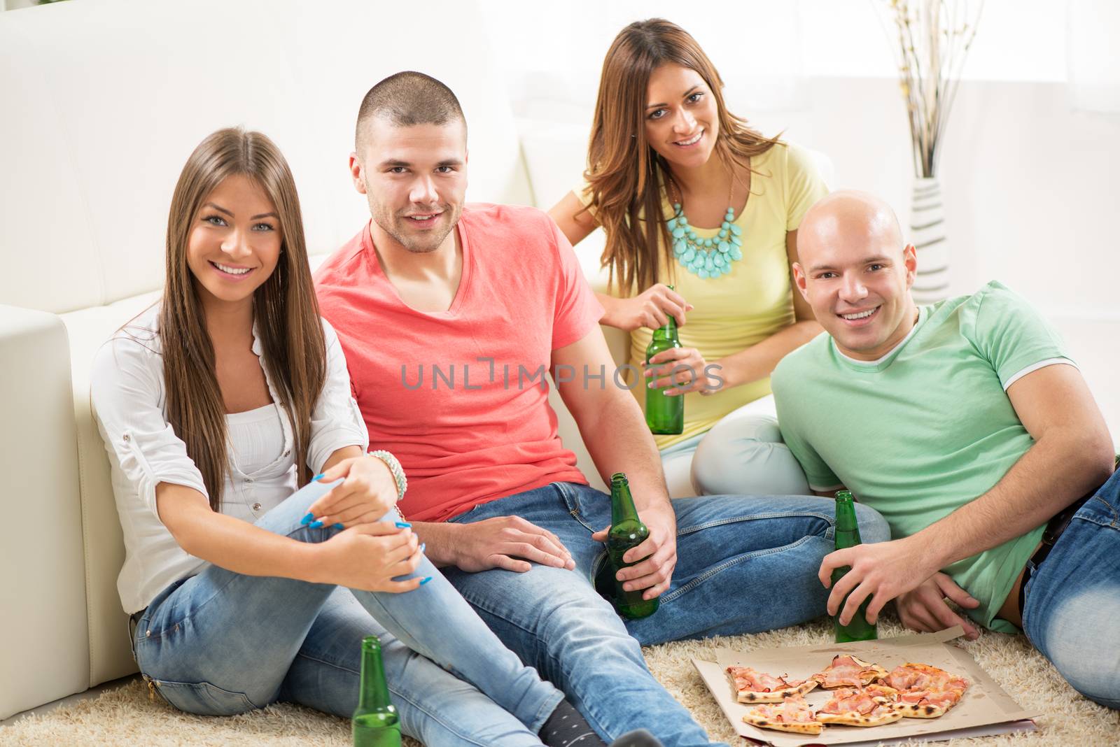 Friends enjoying eating pizza and drink a beer together at home party.