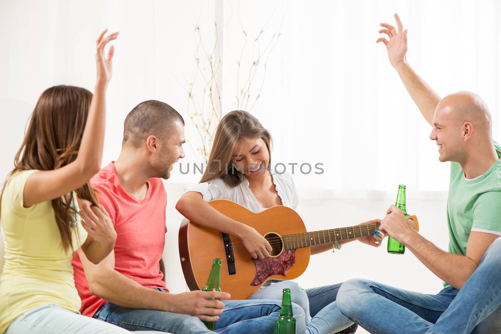 Four friends enjoying with guitar and beer together at the home party.