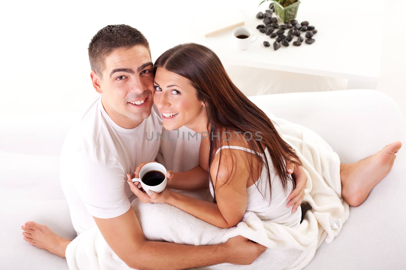 Young romantic couple in love sitting on the bed and drink coffee in the morning