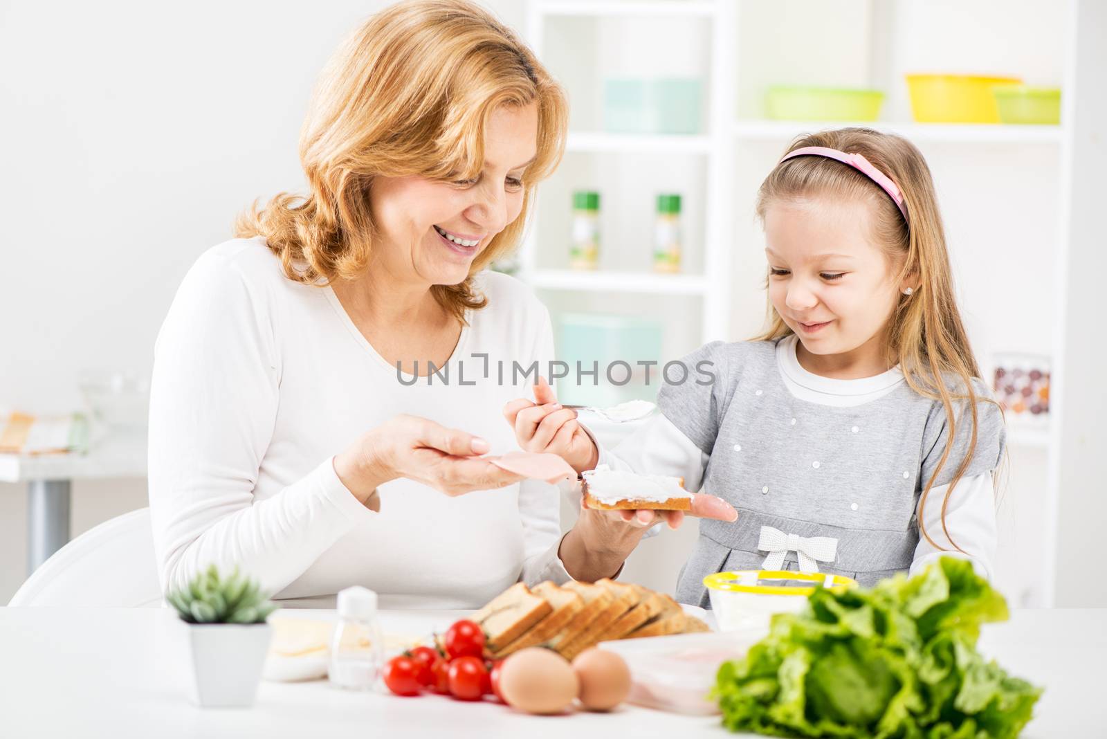 Cute little girl with Beautiful grandmother making a Sandwich in the kitchen.