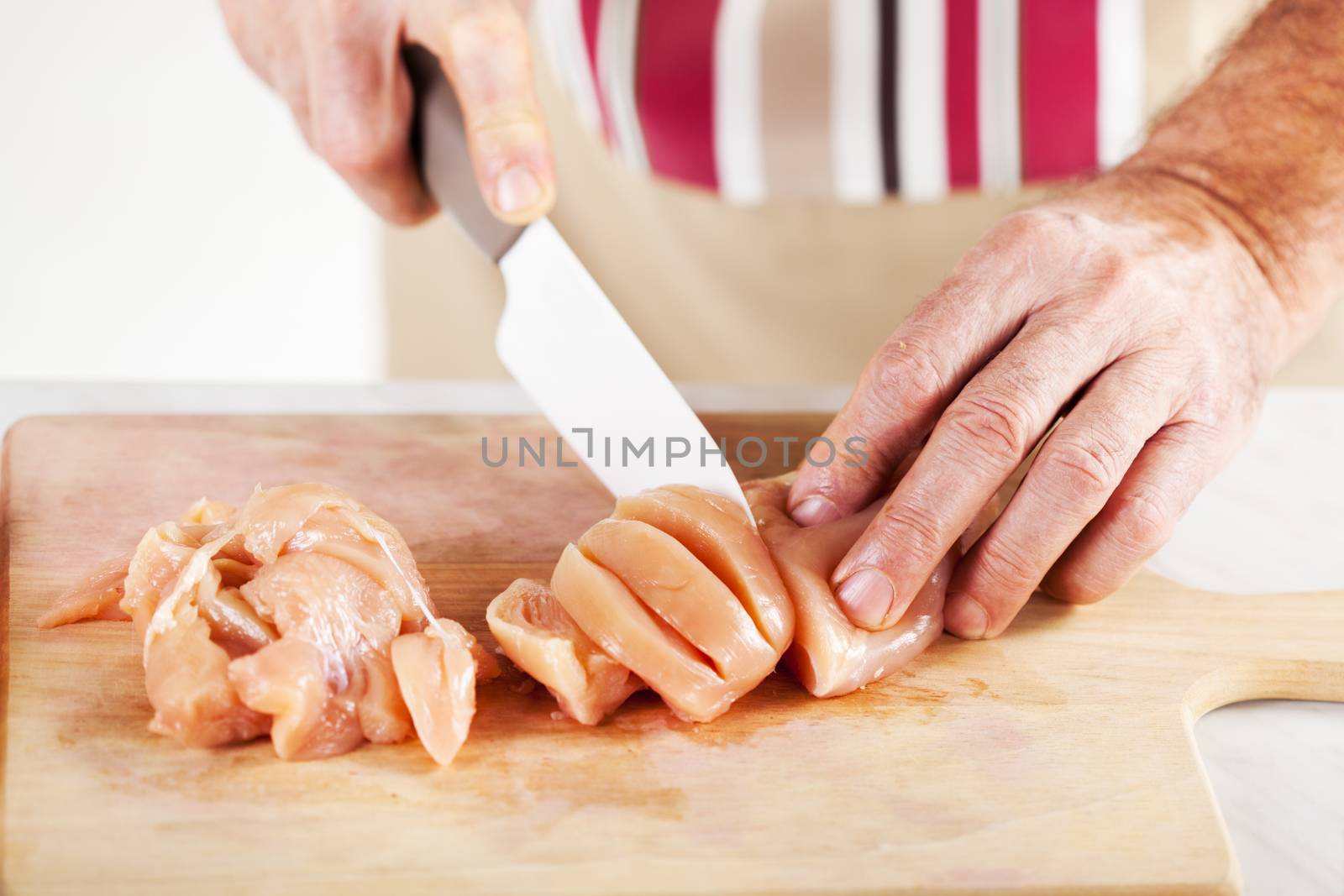 Senior Male Hands Cutting Chicken filet on the kitchen board