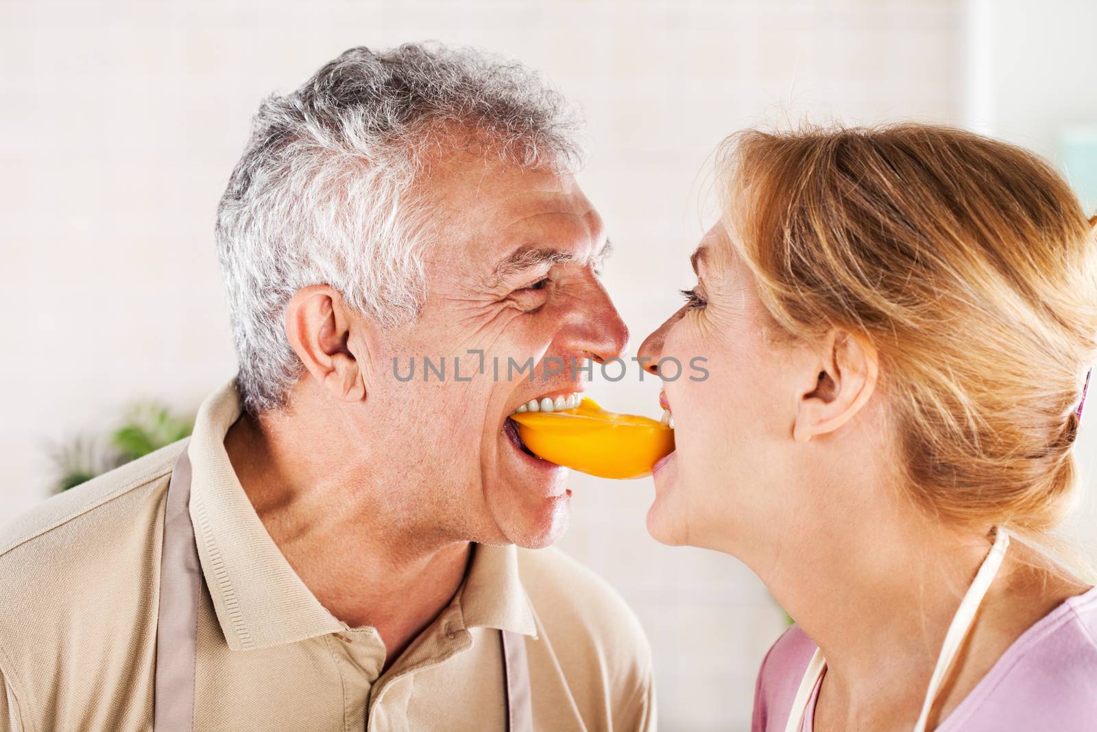 Senior Couple having fun in the kitchen and eating yellow peppers.