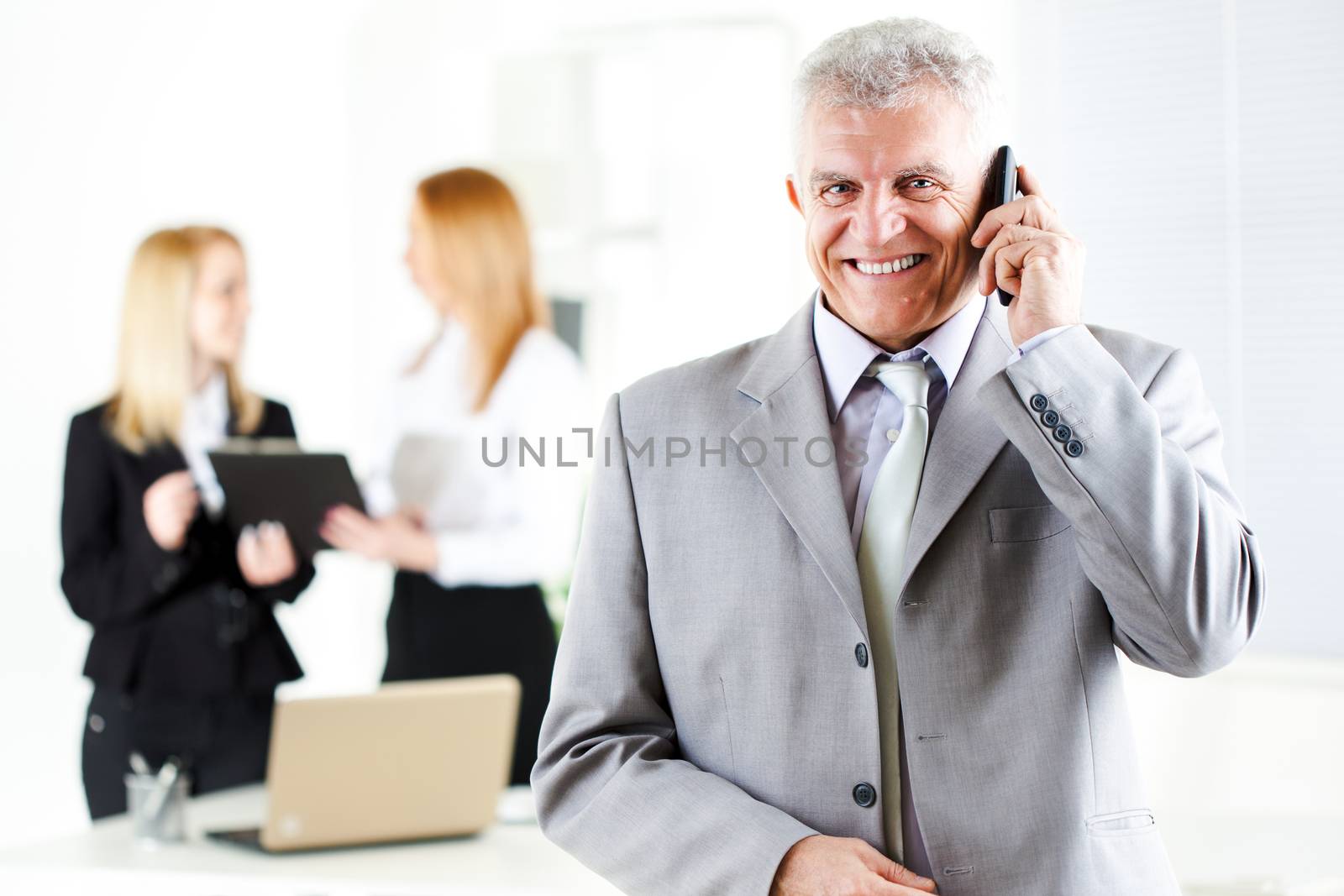 Happy senior businessman talking on mobile phone in the office. Looking at camera. Selective Focus.