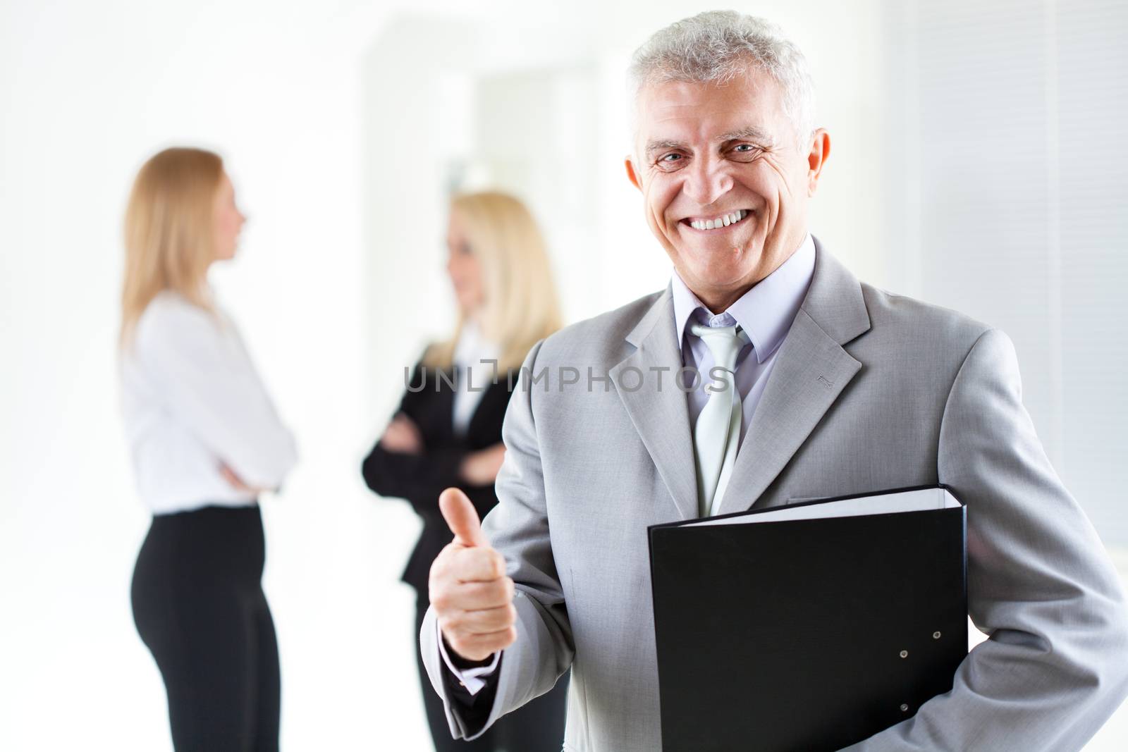 Happy senior businessman with folder in the office, showing thumbs. Looking at camera. Selective Focus.