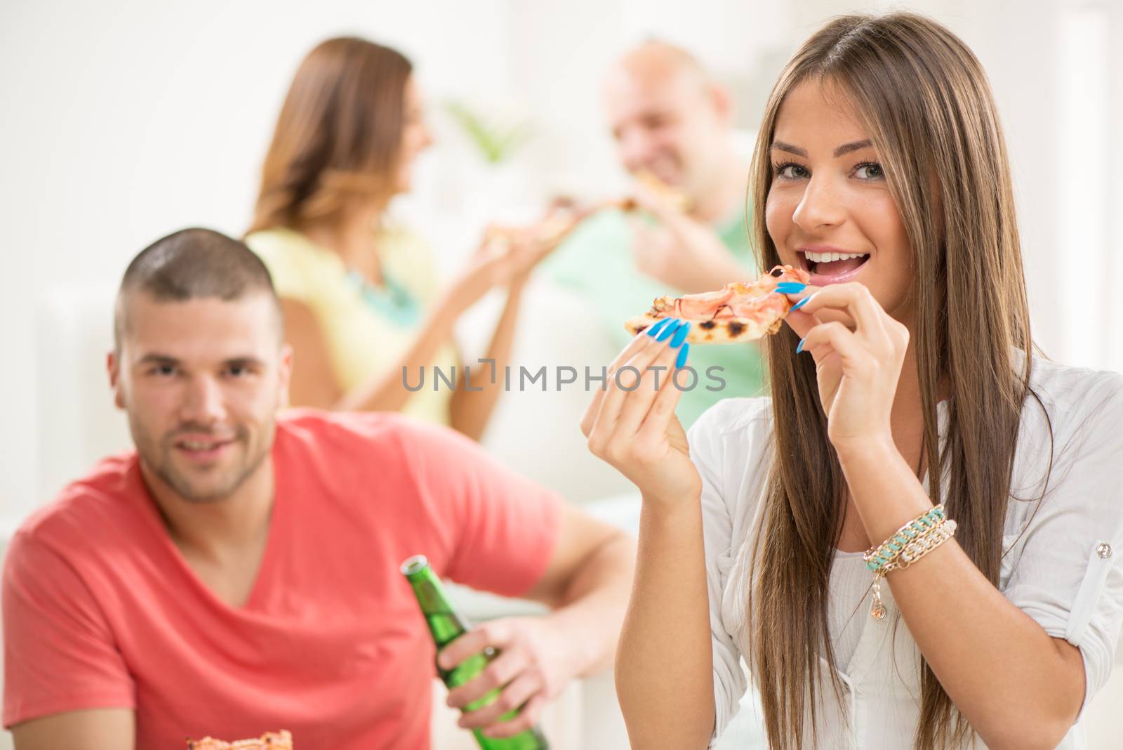 Close up of a young girl smiling and eating pizza with her friends in the background.