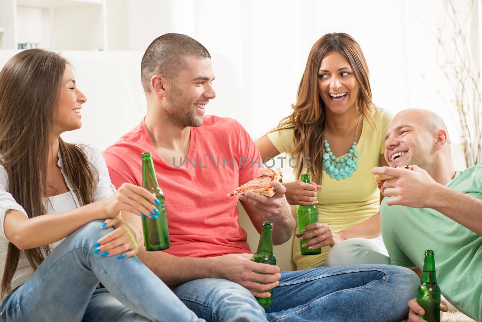 Friends enjoying eating pizza and drink a beer together at home party.