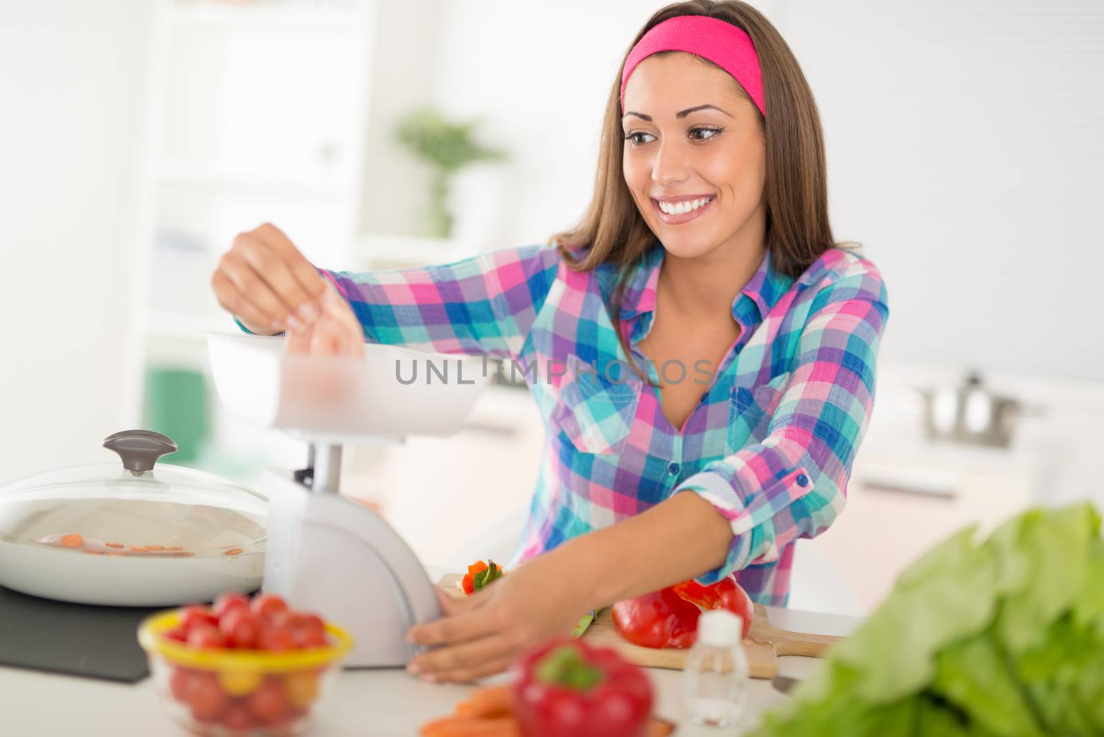 Beautiful young woman making healthy meal in the domestic kitchen. She is weighing meat on kitchen scales.