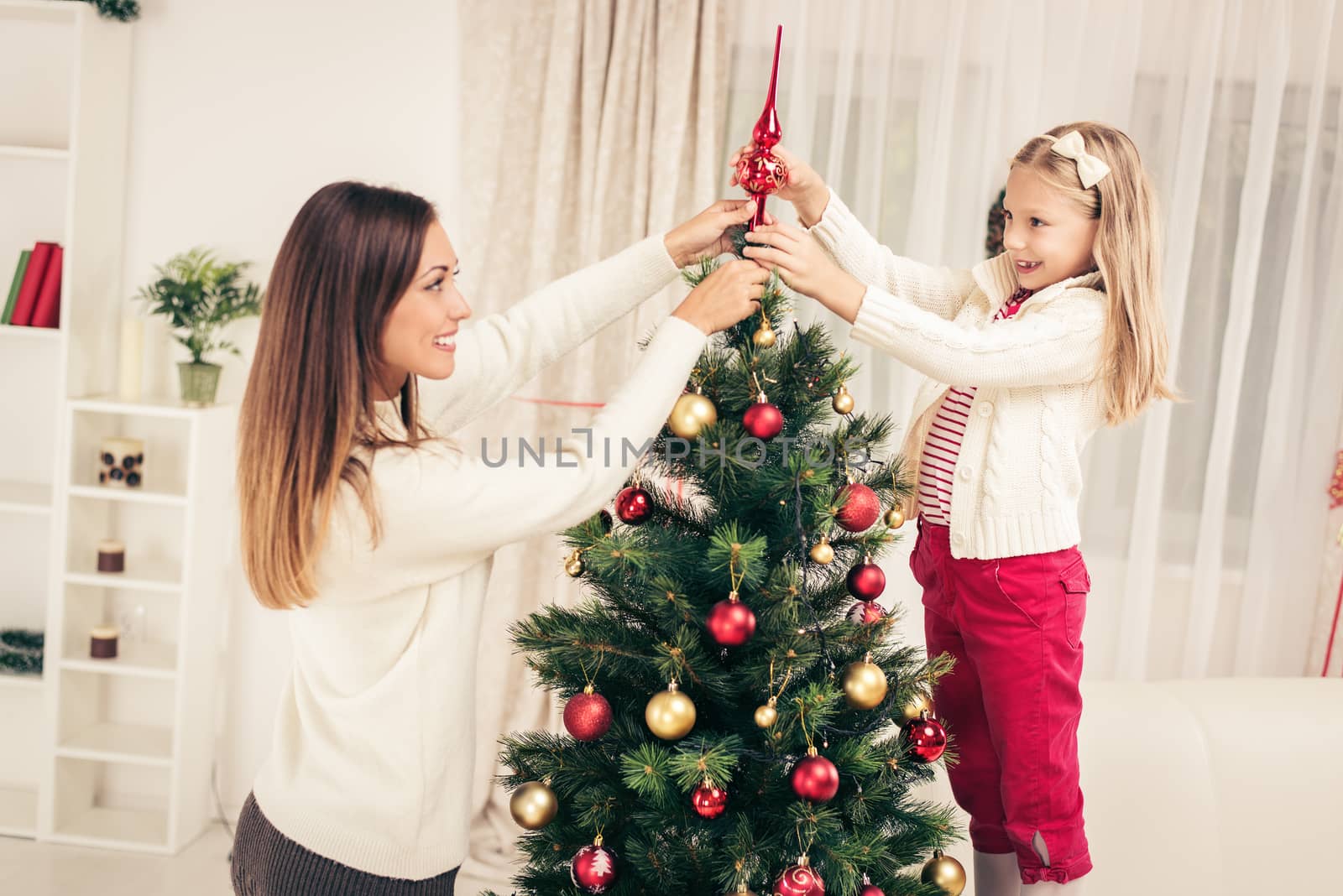 Young mother and her daughter decorating Christmas tree at home. 