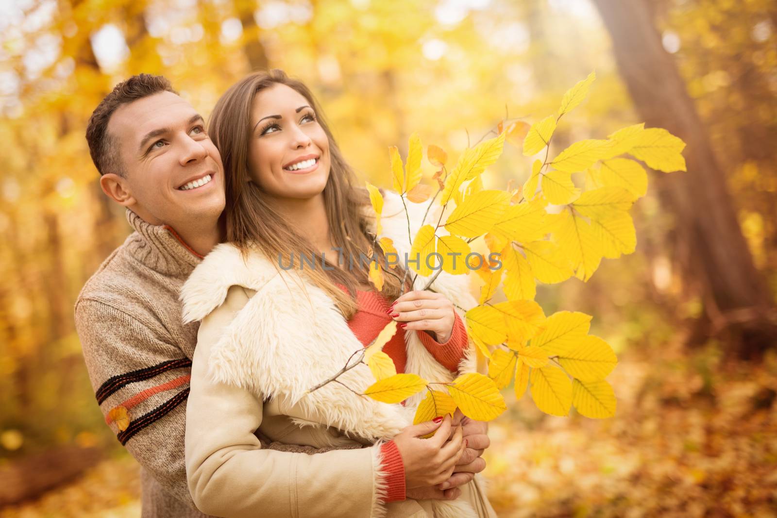 Portrait of a beautiful young couple in sunny forest in autumn colors. They are at embraced and holding yellow leaf.