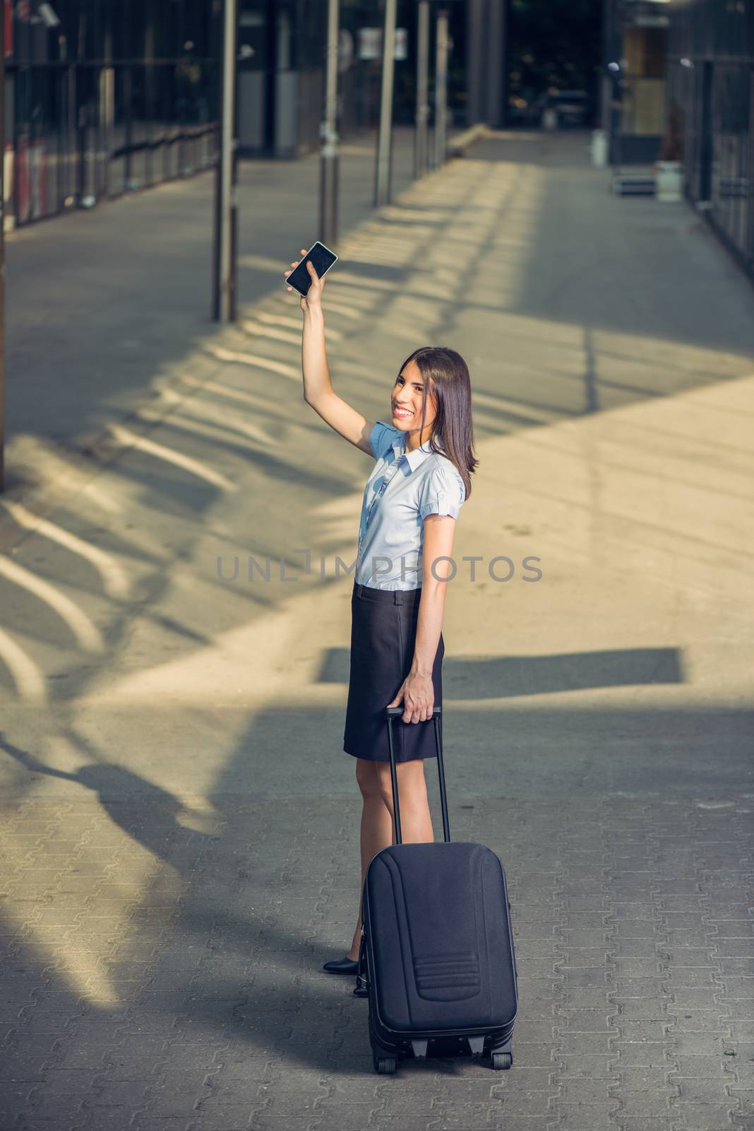Young beautiful business woman walking with suitcase ready for a business trip and waving goodbye on outdoor.