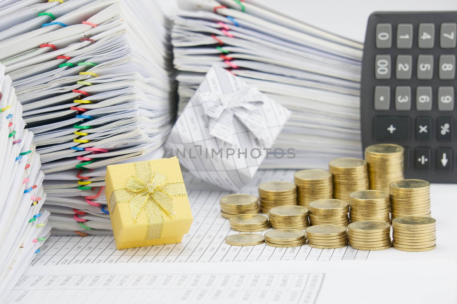 Gold gift box and step pile of gold coins on finance account have blur calculator and pile of paperwork as background.