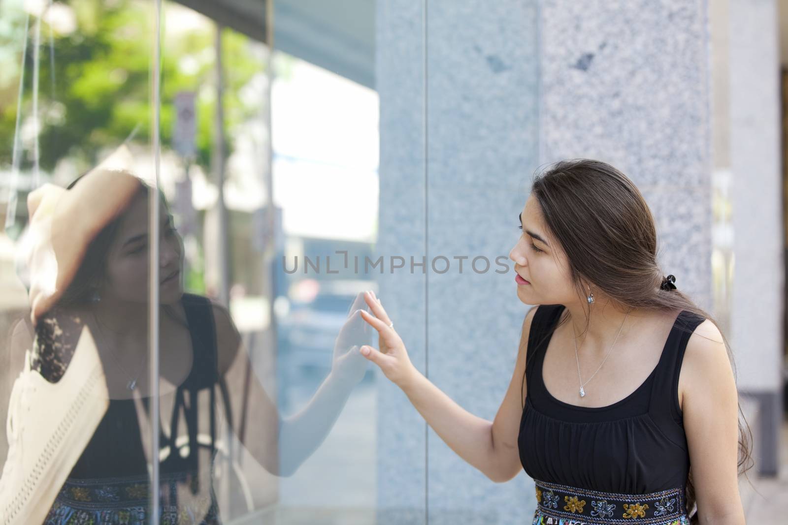 Beautiful biracial Eurasian Asian Caucasian teen girl standing in front of department store window looking in, window shopping