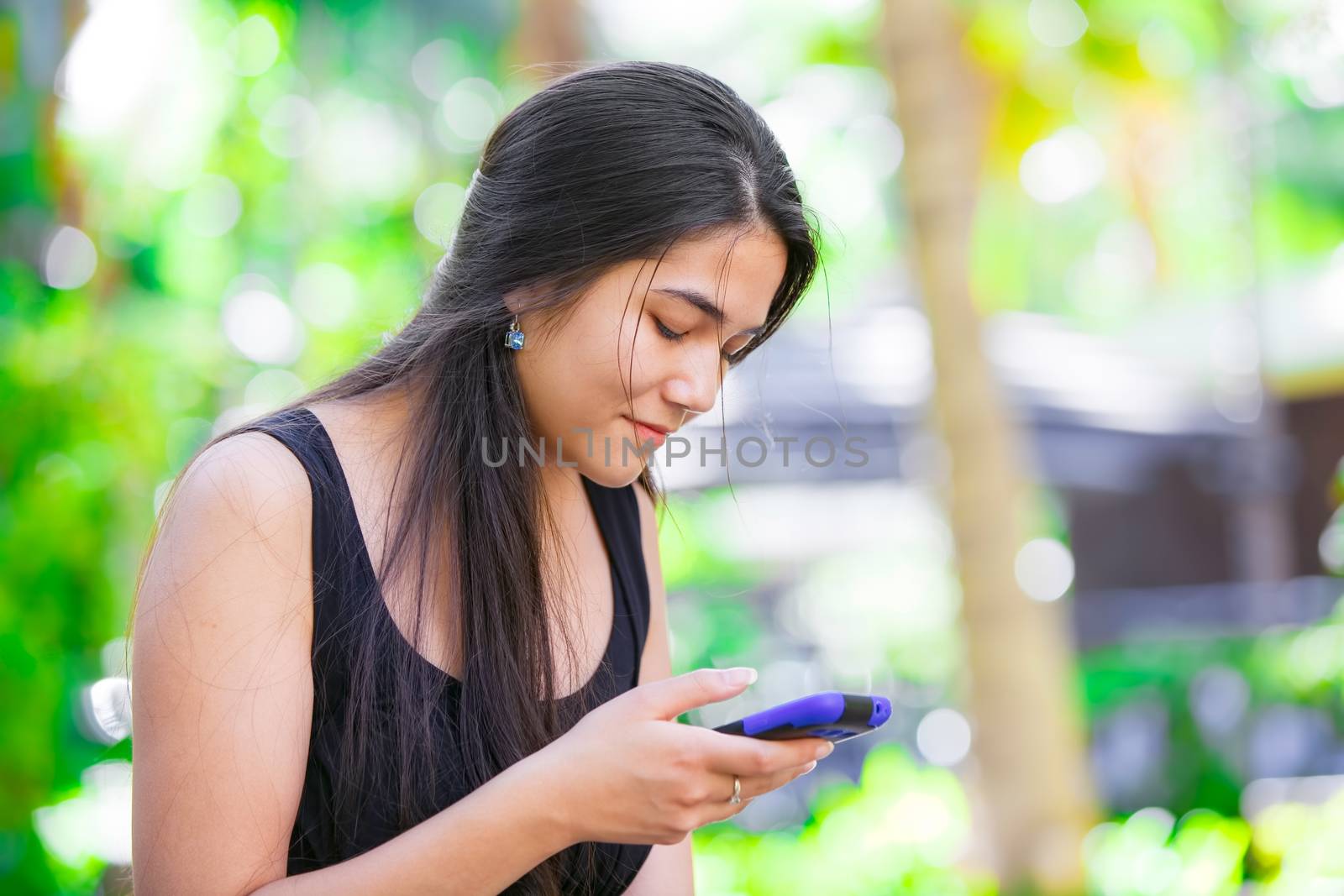 Beautiful biracial Asian Caucasian teen girl talking on cell phone outdoors with green foliage in background