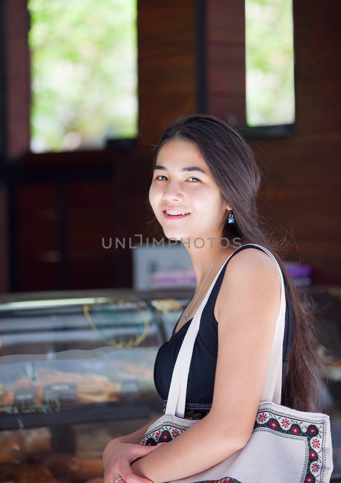 Beautiful biracial Asian, Caucasian, teen girl standing in line at cafe, smiling