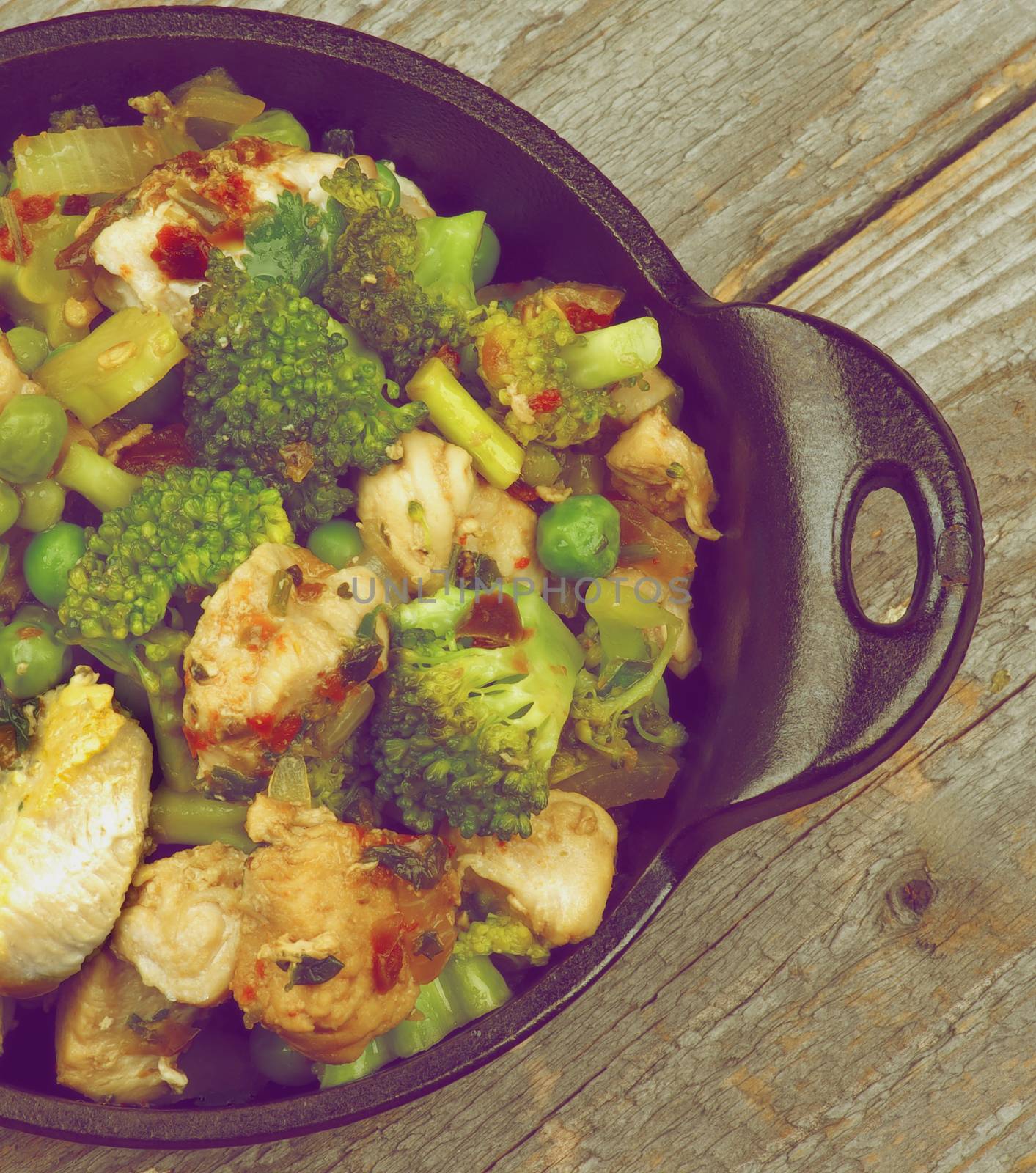 Homemade Chicken Stew with Broccoli, Bell Pepper and Green Pea in Black Saucepan on Rustic Wooden background. Retro Styled