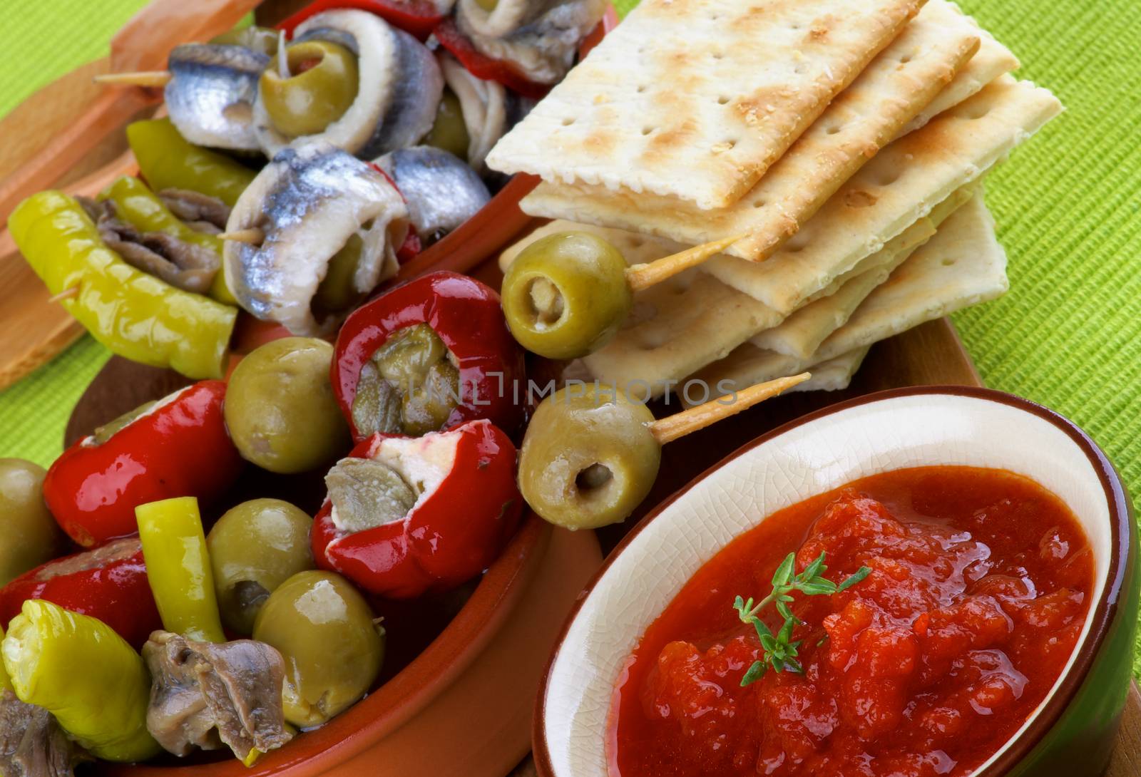 Delicious Spanish Snacks with Tomatoes Sauce, Anchovies, Green Olives, Stuffed Small Peppers and Bread Sticks in Various Bowls closeup on Green Napkin. Focus on Foreground