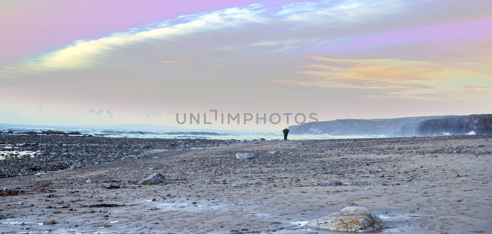 man walking at rocky beach near ballybunion on the wild atlantic way ireland with a beautiful yellow sunset