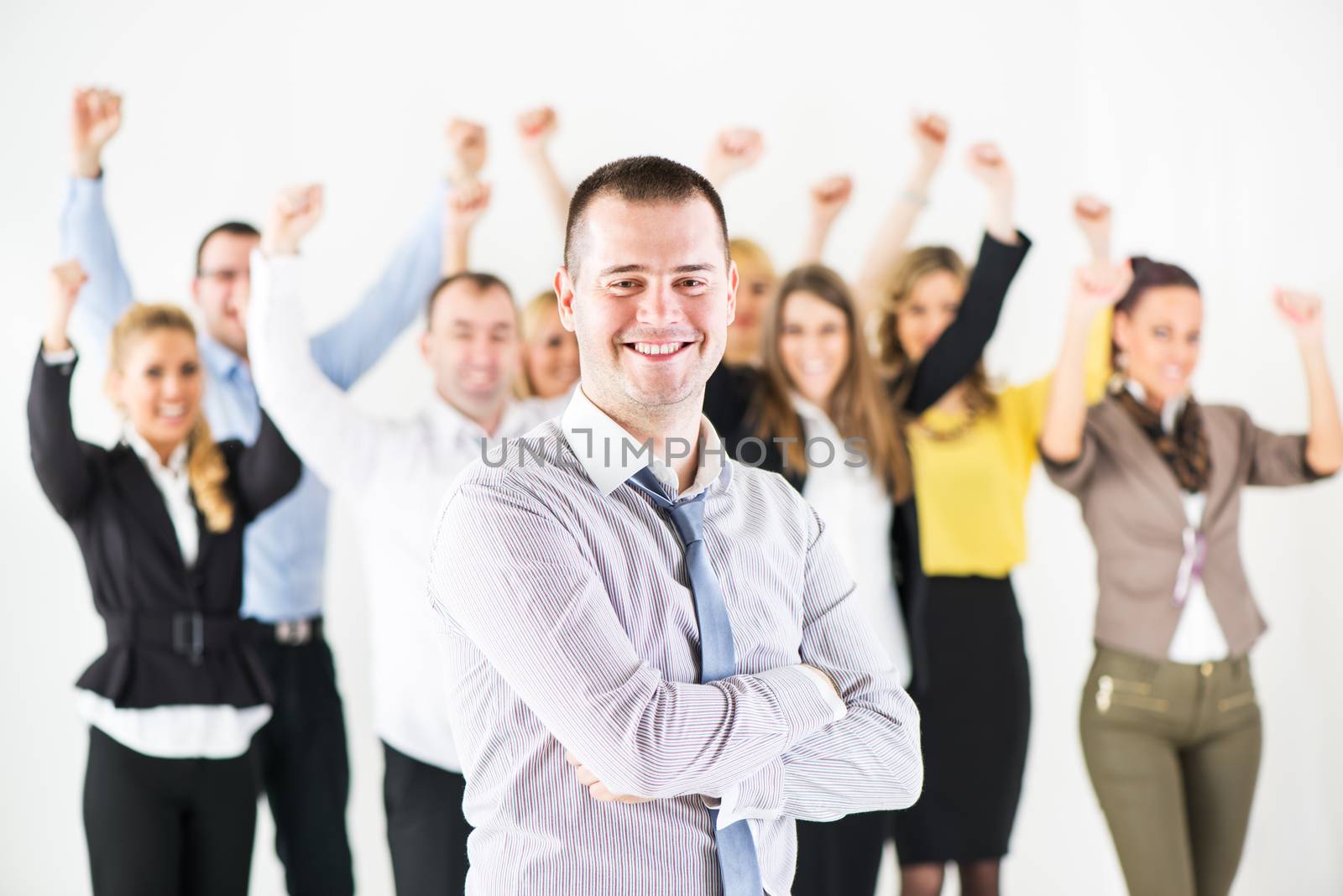 Successful and Smiling businessman with crossed arms standing in front of happy colleagues and looking at the camera.