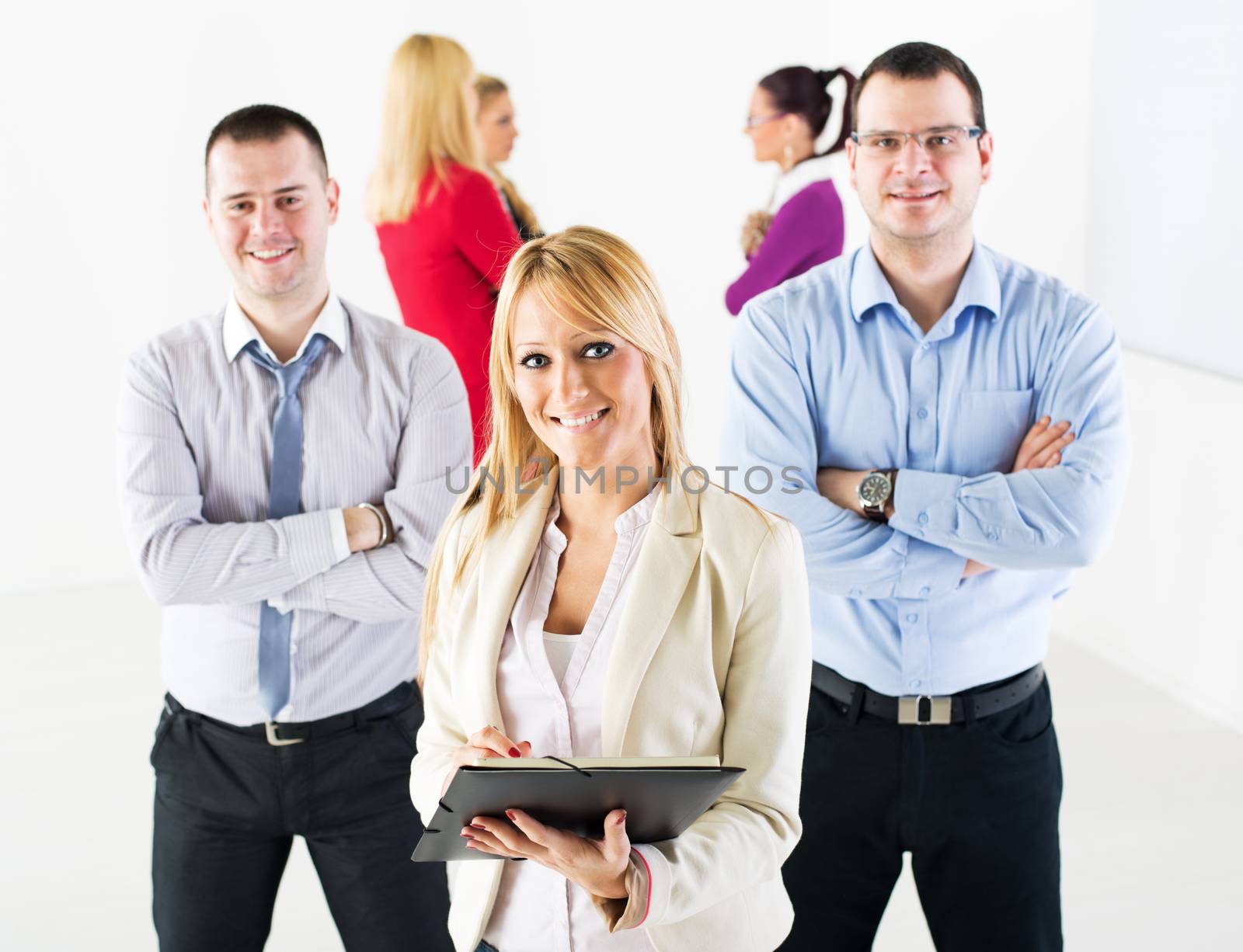 Three smiling co-workers standing in the office in front of their colleague. They are looking at camera.