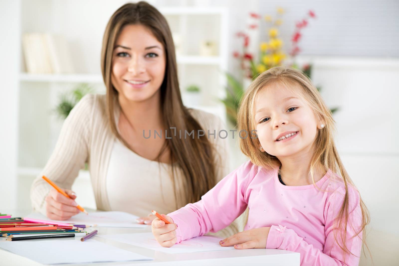 Mother and daughter at home. They drawing with colored pencils.
