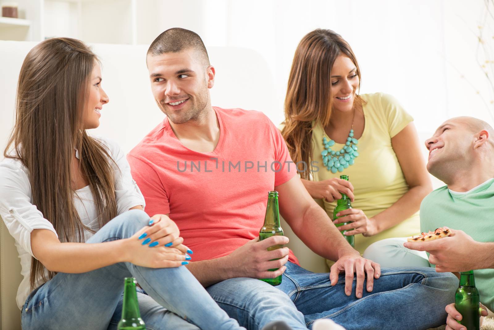 Friends enjoying eating pizza and drink a beer together at home party.