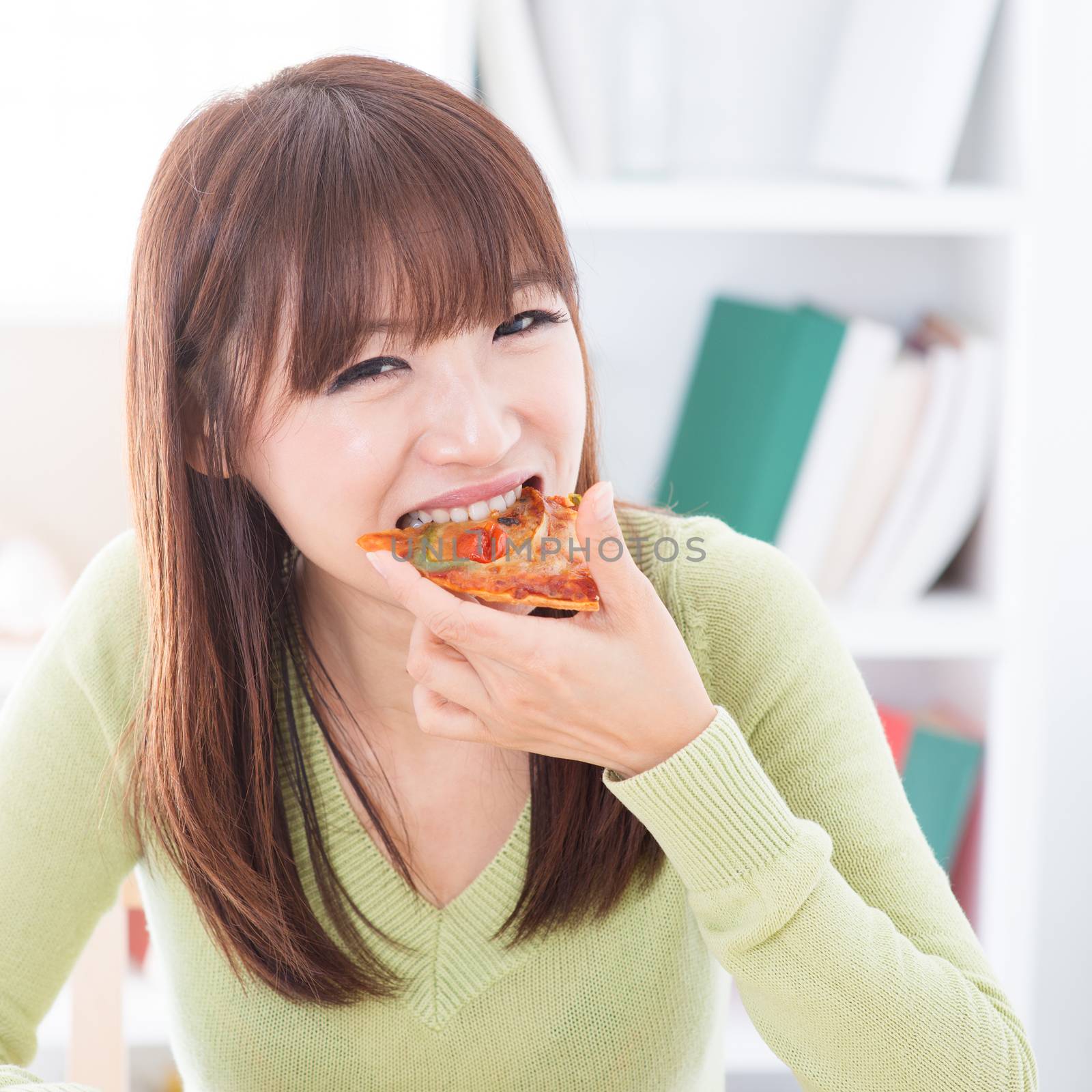 Asian girl eating pizza at home. Female living lifestyle indoors.