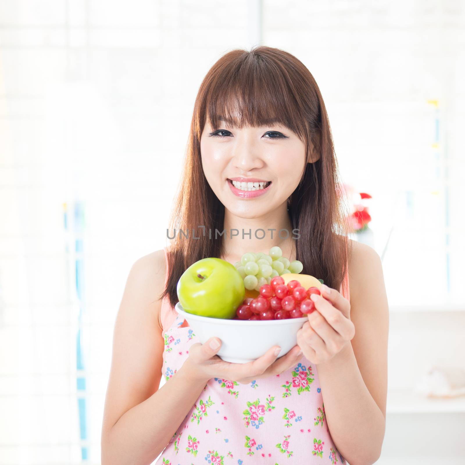 Happy Asian housewife with apron holding fresh fruits. Young woman indoors living lifestyle at home.
