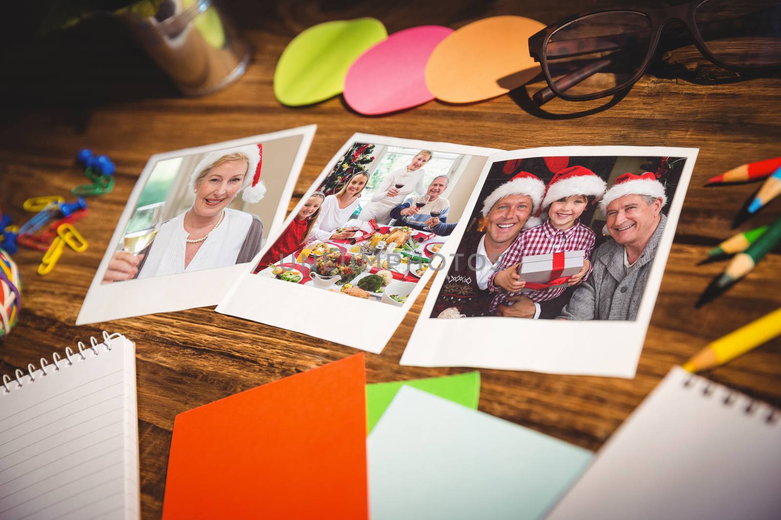 High angle view of office supplies and blank instant photos against smiling mature woman in santa hat toasting with white wine