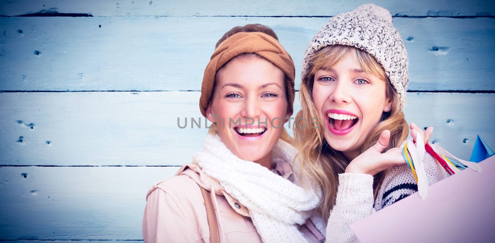 Smiling women looking at camera with shopping bags  against painted blue wooden planks