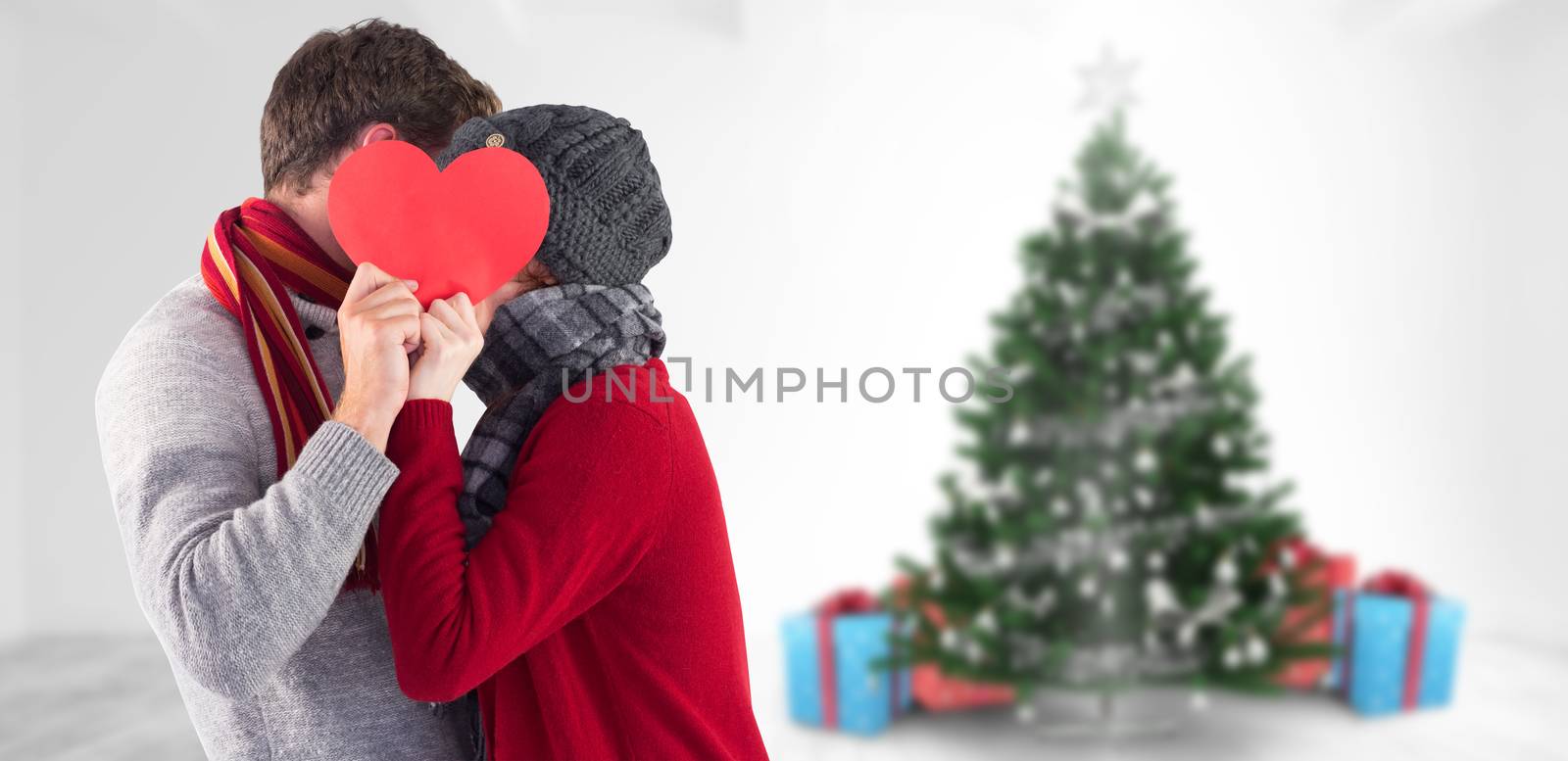 Couple holding a red heart against home with christmas tree